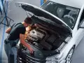Młody mechanik w kombinezonie pracuje przy silniku białego samochodu. To jego pasja, każdy konstruktor marzy o takiej precyzji.