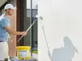 Mann streicht Fassade mit weißer Farbe. Für ein gleichmäßiges Ergebnis ist eine Grundierung notwendig.