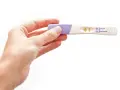 Dłoń trzyma test ciążowy z wynikiem pozytywnym. W okienku widoczny jest symbol plusa, oznaczający ciążę.