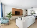 Un elegante salón moderno blanco con sofá, sillón azul, planta y mesa de comedor.