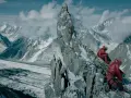 Dwóch wspinaczy w czerwonych kurtkach odpoczywa na skalistej grani. W tle rozciąga się lodowiec i ośnieżone szczyty. To obraz **broad peak tragedia**.