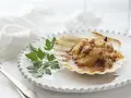 Vieiras gratinadas con tocino y perejil, servidas en su concha sobre un plato blanco.