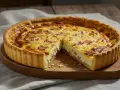 Quiche Lorraine entera con una porción cortada, mostrando su interior cremoso y trozos de tocino.