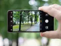 Dłoń trzyma smartfon Huawei P20, aparat kadruje parkowy krajobraz z alejką i drzewami.