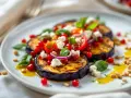 Délicieuse recette avec aubergine grillée, tomates cerises, fromage frais, grenade et pignons de pin. Un plat coloré et savoureux.