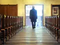 Mann verlässt Kirche in NRW. Er geht durch den Gang zwischen den Kirchenbänken zum Ausgang.
