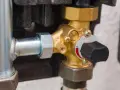 Dettaglio di una valvola pressione acqua caldaia in ottone con manopola nera e indicatore numerico.