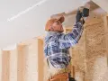 Uomo con trapano installa pannelli per isolamento acustico fai da te sul soffitto di una stanza in costruzione.