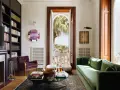 Soggiorno elegante in una casa stile Liberty, con divano verde, poltrona viola, libreria e vista panoramica.