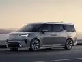 Szary Volvo EM90 jedzie wzdłuż wybrzeża o zachodzie słońca.