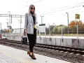 Elegancka kobieta w szarej marynarce i czarnych spodniach czeka na pociąg.