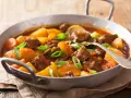 Estofado de ternera tierno con patatas y zanahorias en una sartén, adornado con cebolleta.