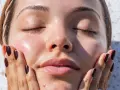 A woman's face, with eyes closed and skin glowing, touches her cheek. It makes you wonder, can your skin type change with the seasons?