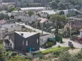 Nowoczesny, czarny dom o trójkątnym kształcie wyróżnia się na tle tradycyjnych terenów mieszkaniowych b. Otoczony zielenią, z niebieskimi drzwiami.