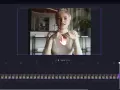 Kobieta w białym golfie, siedząca i mówiąca, z dłonią wskazującą na ekran edytora wideo.