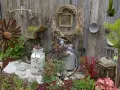 Kreative Gartendeko Ideen: altes Fahrrad mit Blumen, Milchkannen, Rostblume und Schreibmaschine vor Holzzaun.