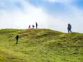 Famiglia esplora sentieri per bambini su una collina verdeggiante sotto un cielo azzurro e nuvoloso.