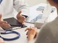 Lekarz omawia z pacjentem diagnozę, być może f43 kod choroby. Na stole stetoskop i laptop.