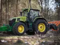 Zielony traktor John Deere z pomarańczowym mulczerem, gotowy do pracy w lesie.