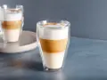 Dwa latte macchiato w szklankach z podwójnymi ściankami, z wyraźnie widocznymi warstwami mleka i kawy.