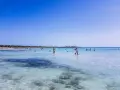 Słoneczny dzień na plaży Es Trenc. Ludzie kąpią się w krystalicznie czystej wodzie, ciesząc się wakacjami.