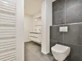 Salle de bain moderne avec wc suspendu, carrelage gris anthracite et blanc, lavabo suspendu et radiateur blanc.