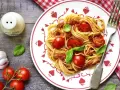 Makaron spaghetti z sosem pomidorowym, pomidorkami koktajlowymi i bazylią na talerzu.