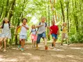 Des enfants joyeux, des supernova juniors, courent sur un sentier forestier ensoleillé, pleins d'énergie.