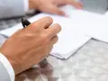 Dłoń z długopisem nad dokumentem, przygotowująca się do podpisania umowy przyrzeczonej.