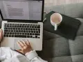 Person arbetar på laptop i soffan, en kopp står bredvid. Perfekt för dig som söker bra utbildningar på distans.