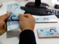 Ręce liczą banknoty 10 dinarów, tunezyjska waluta. Na stole leżą stosy pieniędzy, a w tle widać klawiaturę komputera.