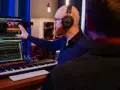 Tontechniker mit Kopfhörern erklärt seinem Kollegen am Mischpult die Einstellungen. Er bittet um Feedback zur Abmischung.