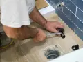 A person uses a wrench to tighten a toilet flange bolt, demonstrating how to replace a toilet flange.