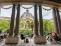 Vue sur le Grand Palais depuis un portique, avec des visiteurs profitant d'un café dans le jardin. Un petit palais, un grand palais.