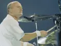 Phil Collins, w białej koszuli, gra na perkusji. Legendarny muzyk, znany z zespołu Genesis.