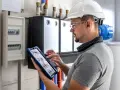 Elektryk w kasku i okularach ochronnych dokonuje przeglądu instalacji elektrycznej, korzystając z tabletu.