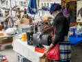 Frau mit Tätowierungen auf dem Arm sucht auf einem antik flohmarkt nach Schätzen. Sie hält eine rote Tasche.