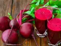 Frische rote Bete und zwei Gläser mit leuchtend rotem Rote-Bete-Saft stehen auf einem Holztisch.