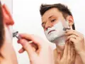Hombre con espuma de afeitar en la cara, afeitándose con una maquinilla. ¿Es mejor afeitarse antes o después de la ducha?