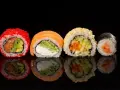 Różne rodzaje sushi: rolka z łososiem i awokado w ikrze, z łososiem i serkiem, z sezamem i warzywami, oraz klasyczne maki z łososiem.