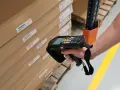 Mano escaneando cajas apiladas con un dispositivo, usando la **fórmula de Wilson** para optimizar el inventario.