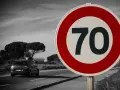 Segnale 226: limite di velocità 70. Un'auto viaggia su una strada panoramica.