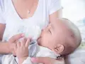 Dziecko pije mleko modyfikowane z butelki. Mama karmi maluszka.