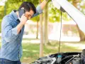 Mann telefoniert neben offenem Motorraum. Was ist beim Abschleppen zu beachten bei PKW Defekt?