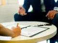 Dłoń podpisuje dokument, podczas gdy mężczyzna w garniturze gestykuluje. Może to być umowa, która pozwoli uniknąć kary UFG.