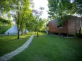 Malowniczy camping w Albanii z białymi namiotami typu bell i drewnianym domkiem na palach, otoczony zielenią.