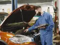 Mechanik z komputerem diagnostycznym sprawdza silnik pomarańczowego auta. Zastanawiasz się, ile trwa wymiana oleju?