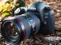 Profesjonalny aparat Canon EOS 5D Mark IV z obiektywem leży na leśnym podłożu.