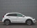Biały Kia Niro EV widziany z boku na tle szarej, falistej ściany.