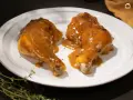 Dos jugosas piernas de pollo a la mostaza, cubiertas con una salsa dorada y espolvoreadas con hierbas, servidas en un plato blanco.